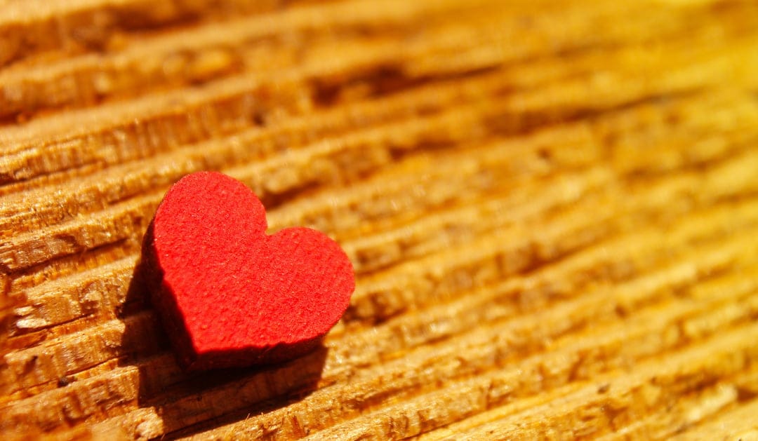 Red heart ornament sits on a rustic wooden surface with deep brown grain and diagonal textured plank lines.