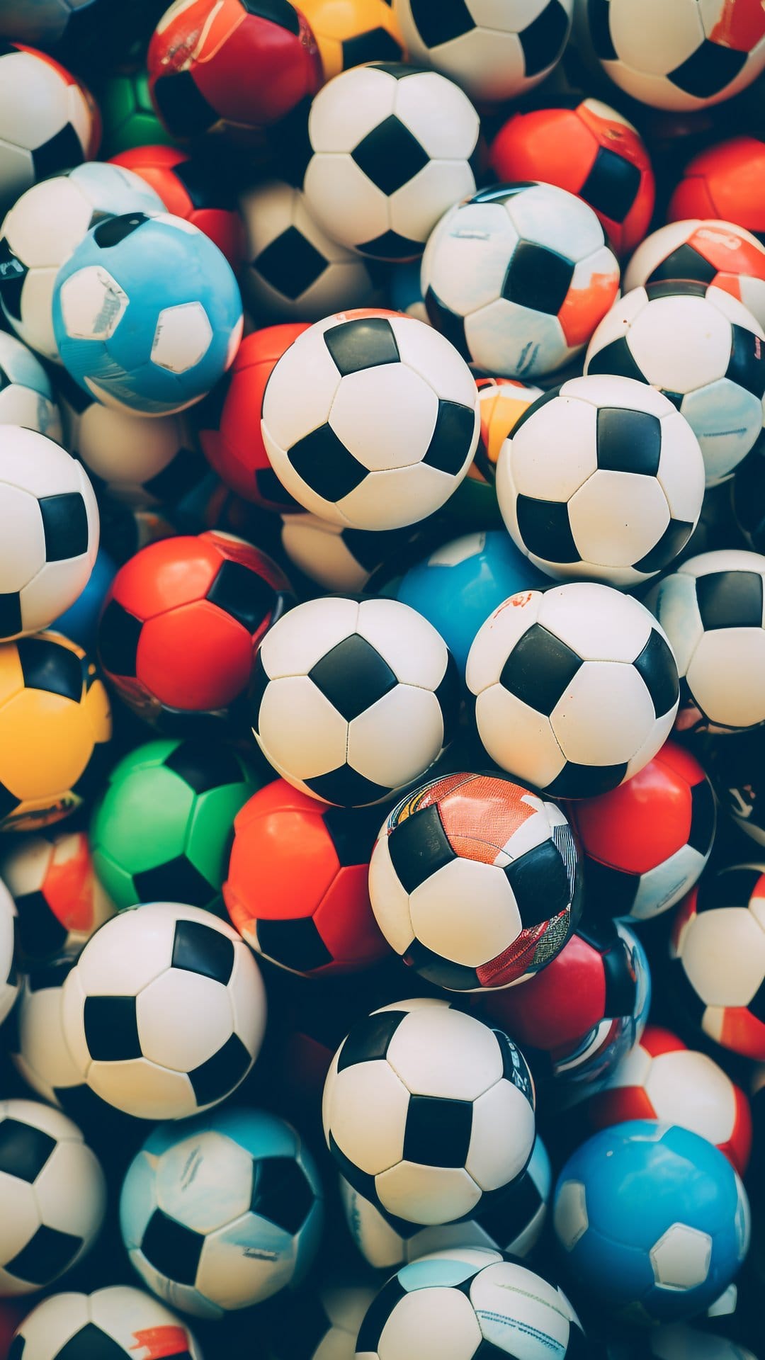 Soccer balls in various colors like red, blue, and yellow are tightly stacked in a close-up macro view.