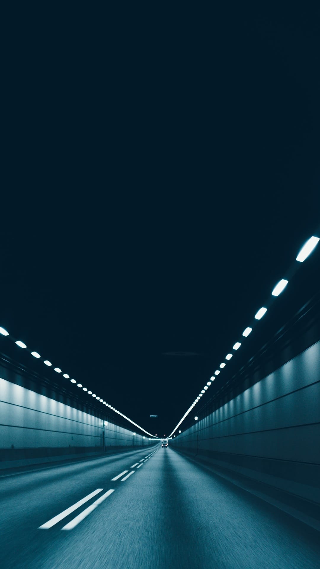 Parallel white lights illuminate a sleek dark underground road in a deep perspective composition for mobile.
