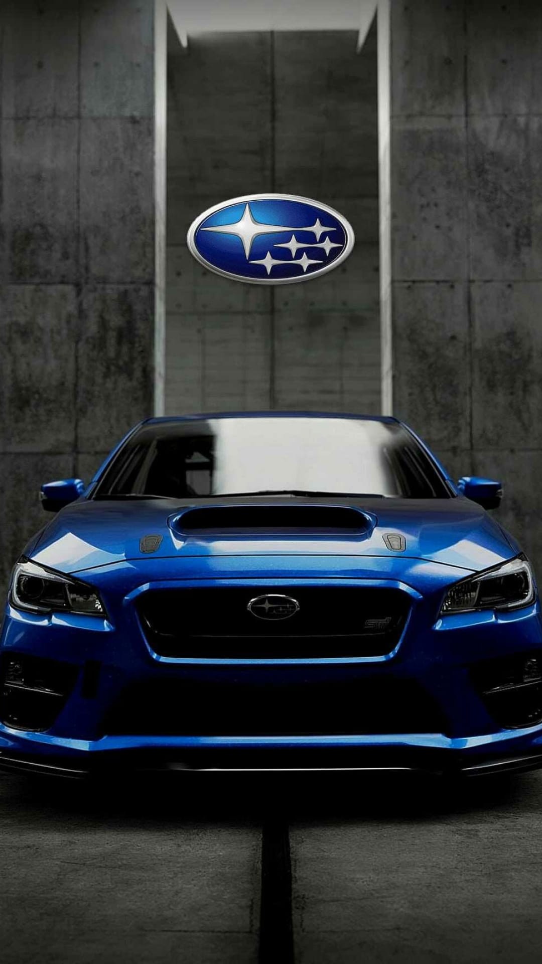 Blue Subaru WRX STI front view with an aggressive hood scoop and LED headlights against a textured concrete wall.
