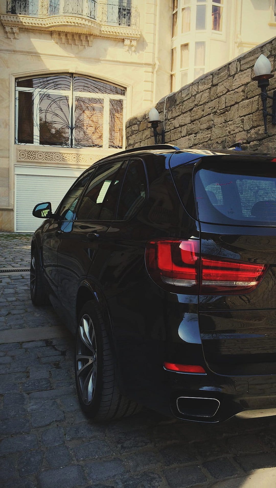 Rear of a black BMW SUV parked on a cobblestone street with a historic stone building in the background.