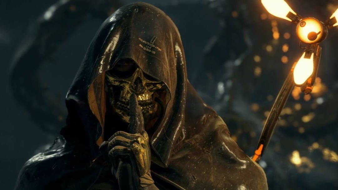 Higgs Monaghan wearing a golden skull mask and hooded cloak with a glowing Odradek scanner in a dark setting.