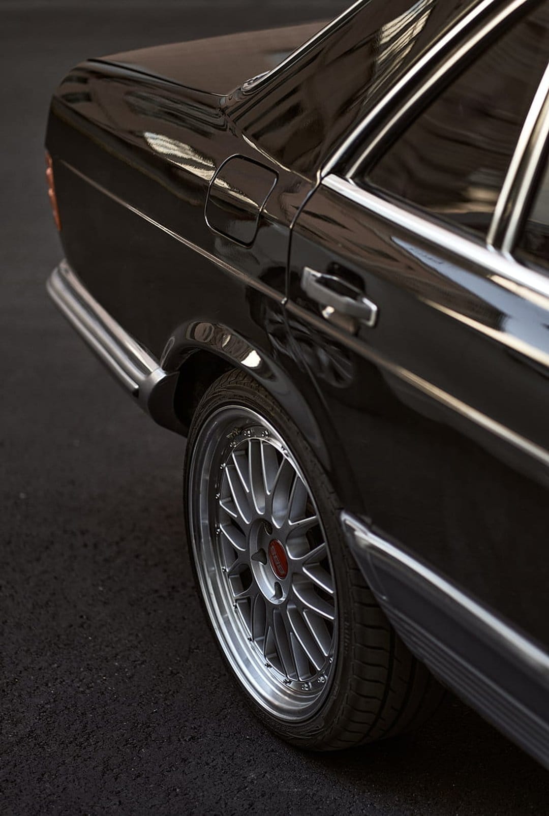 Mercedes alloy wheel and chrome trim on a black classic sedan highlight the rear body panel and asphalt.
