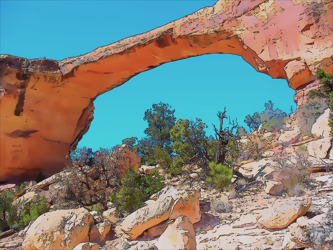 Massive sandstone arch spans a clear blue sky above rocky desert terrain with scattered green scrub brush.