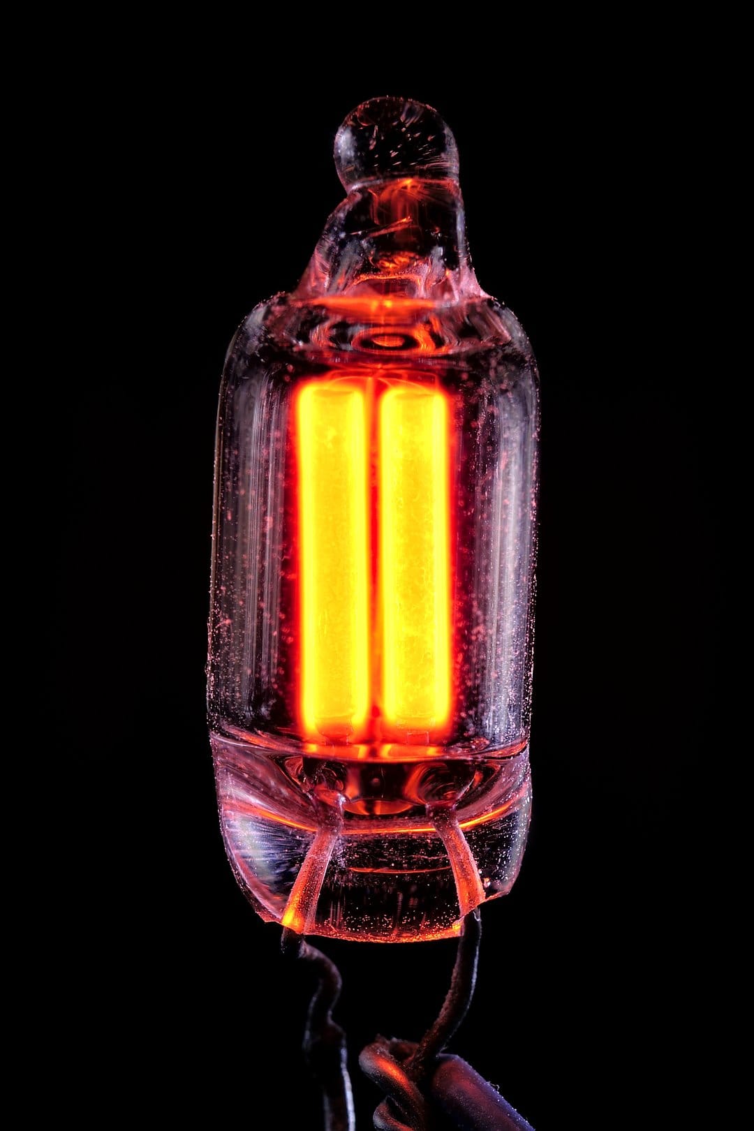Amber neon gas discharge lamp glowing with internal electrodes against a dark background in a macro photograph.