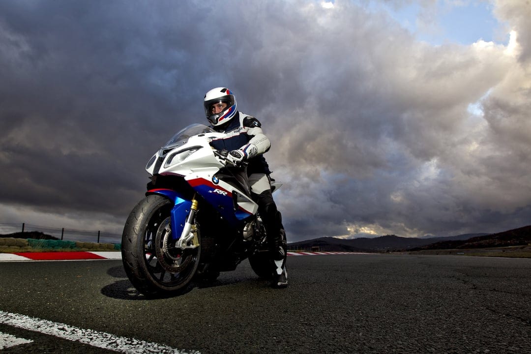BMW S1000RR sportbike with a rider on a racetrack under dramatic clouds and cinematic lighting.