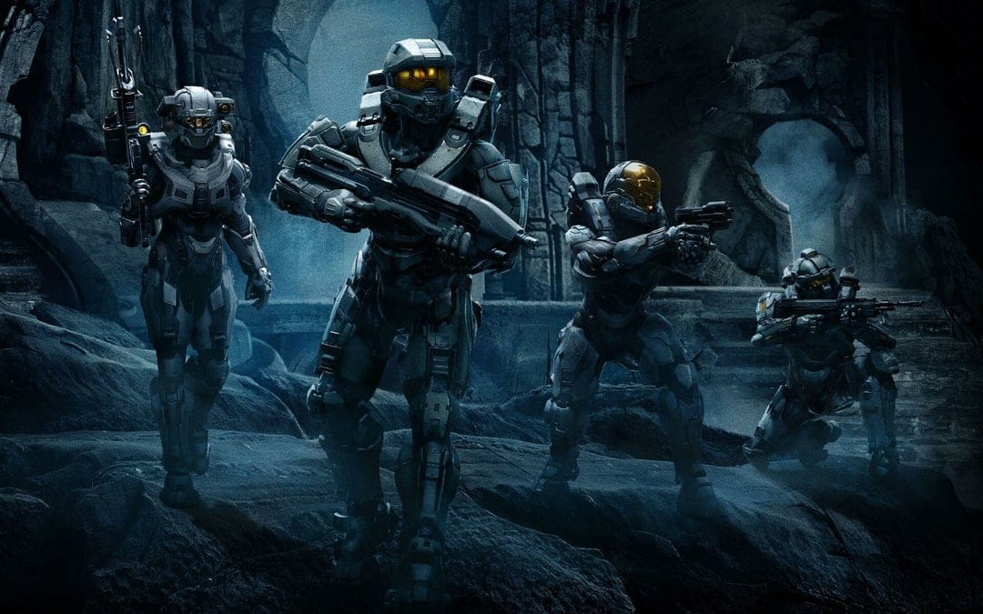 Armored Spartan soldiers moving through dark rocky ruins with tactical rifles under cinematic blue light.