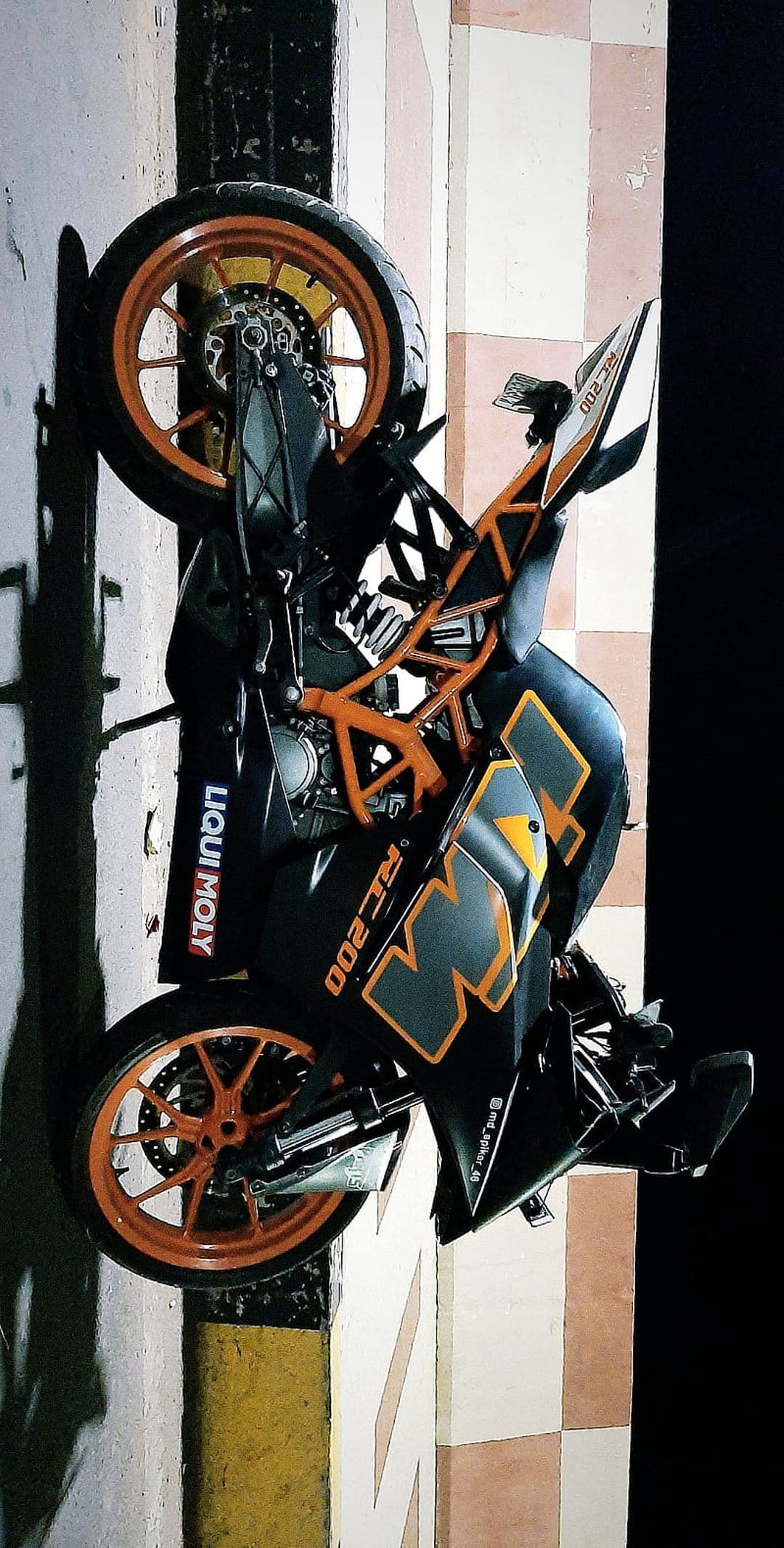KTM RC 200 sportbike with orange rims and Liqui Moly decals parked on a beige checkered tile floor.