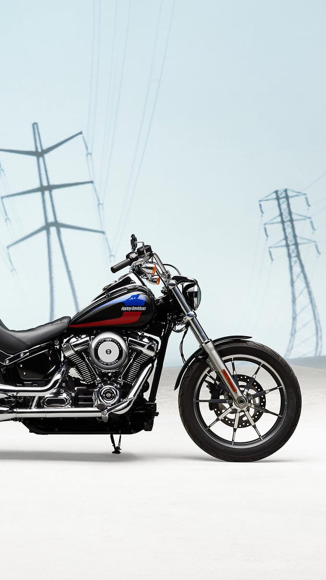 Harley Davidson motorcycle with a black fuel tank parked in front of tall industrial electrical power lines.