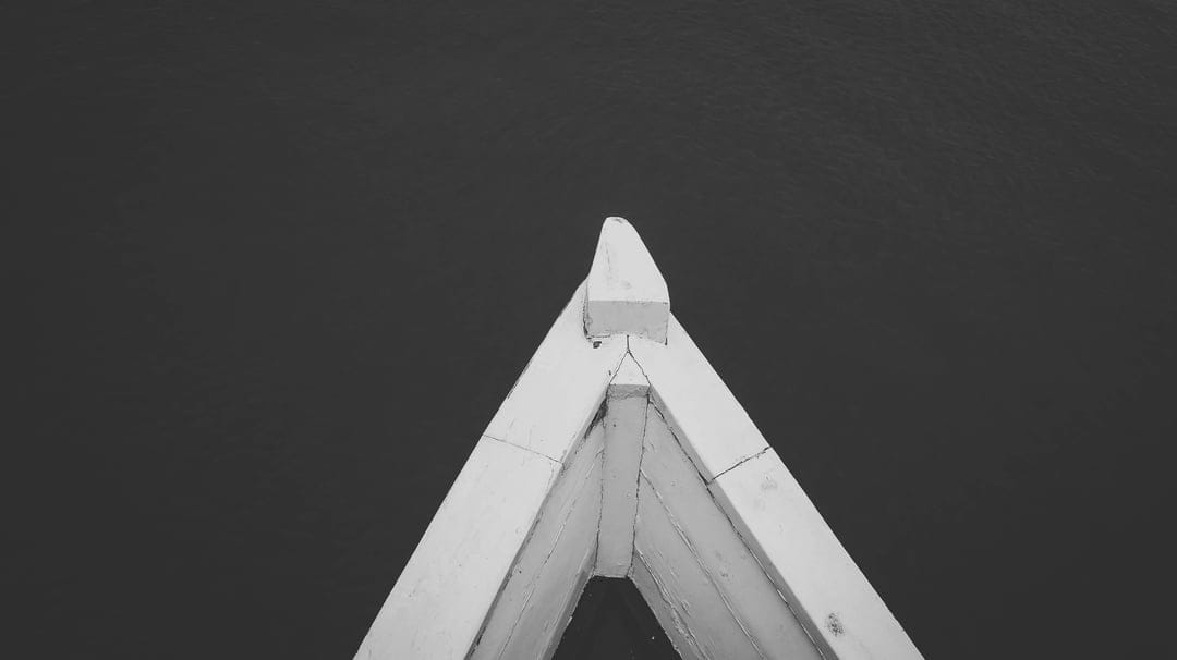 White wooden boat bow cutting through dark, rippled water in a high-contrast minimalist vertical composition.