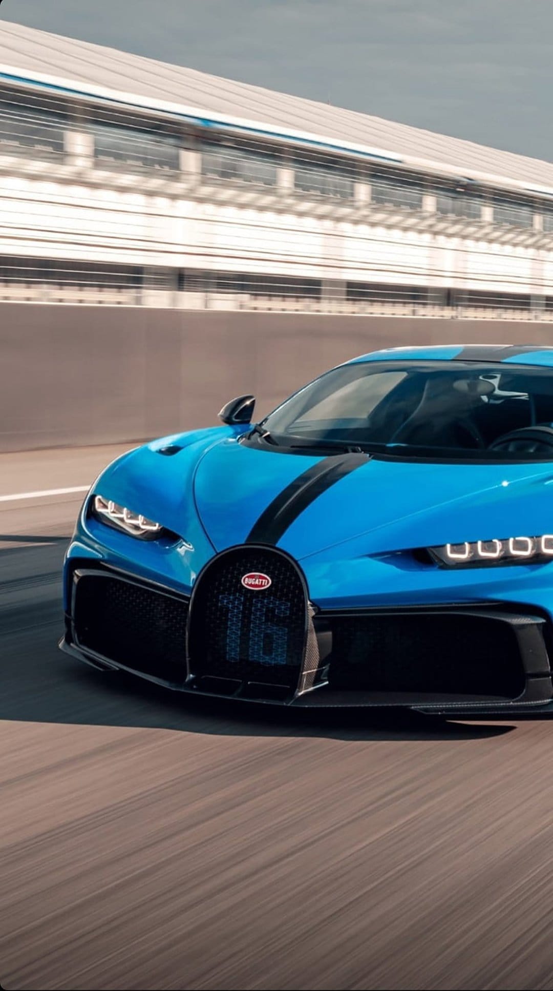 Blue Bugatti Chiron Super Sport 300+ with black stripes racing on a grey asphalt track during the day.