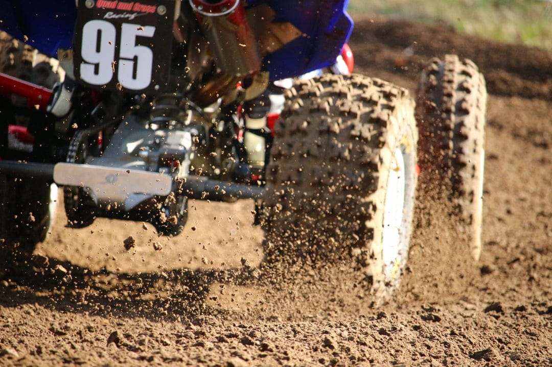 ATV with number 95 racing on a dirt track while spraying thick mud and debris from spinning knobby tires.