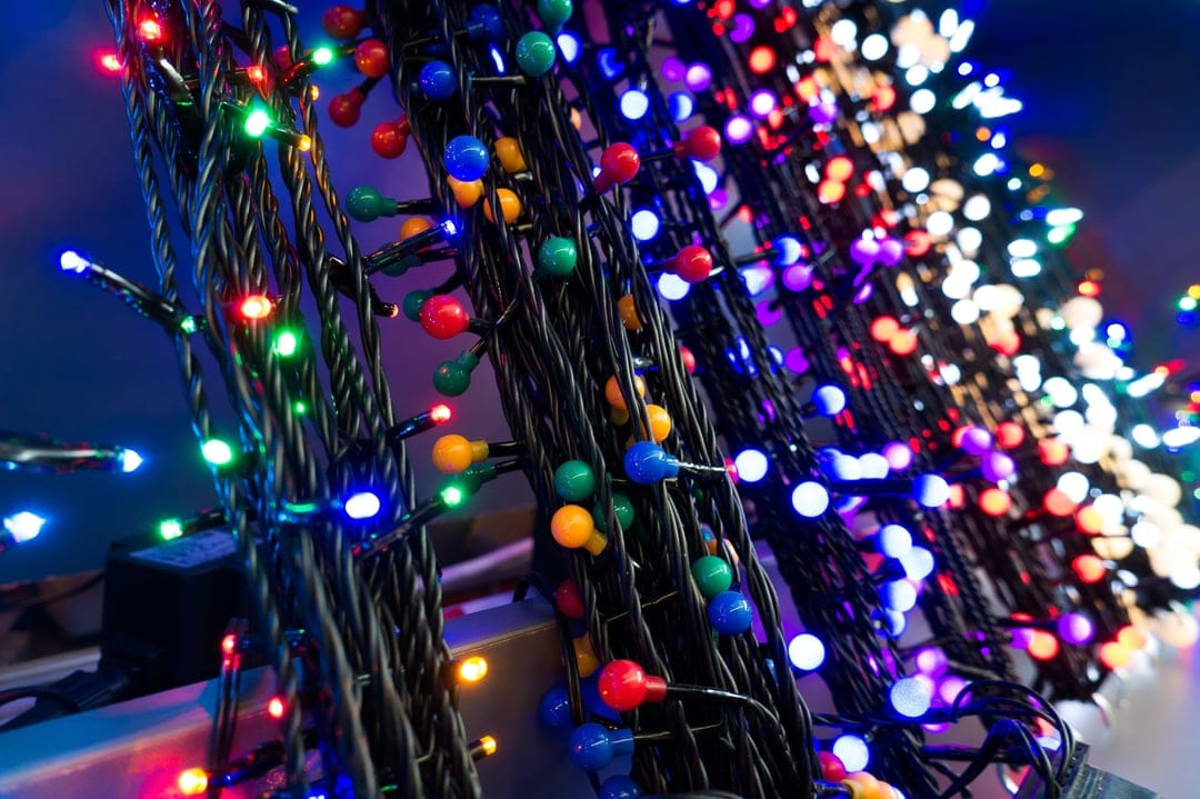 Vibrant red, green, and blue LED holiday lights are tightly coiled around a dark textured electrical cable.
