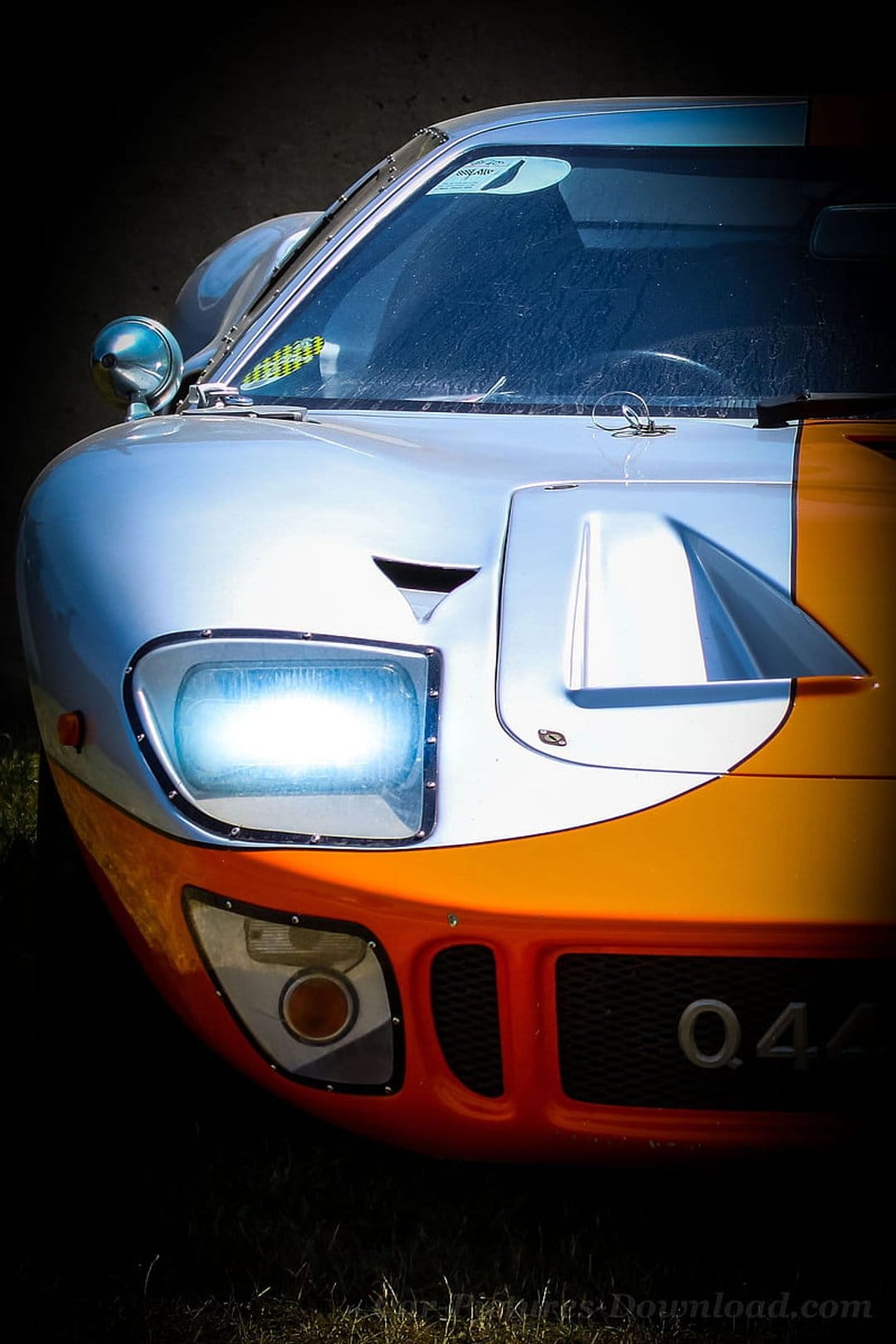 Ford GT40 headlight and silver bodywork with orange racing stripes in a detailed front-angle close-up view.
