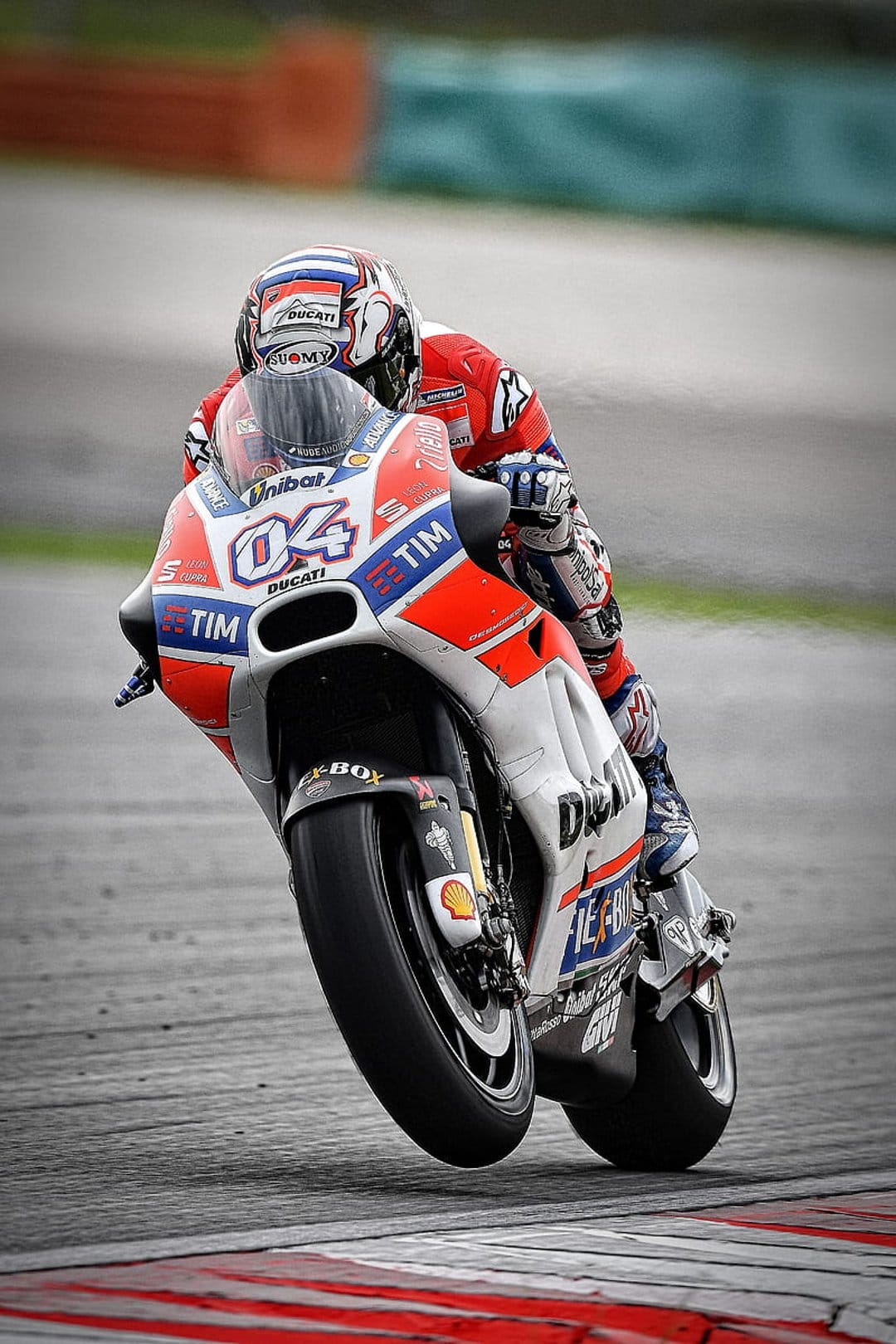 Andrea Dovizioso leans a red and white Ducati motorcycle into a sharp turn during a professional MotoGP race.