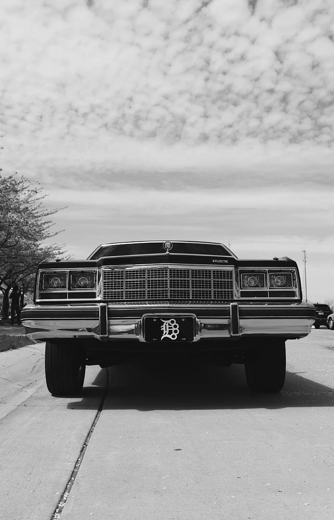 Vintage black Buick front with chrome grille and a Detroit D emblem on the license plate under a cloudy sky.