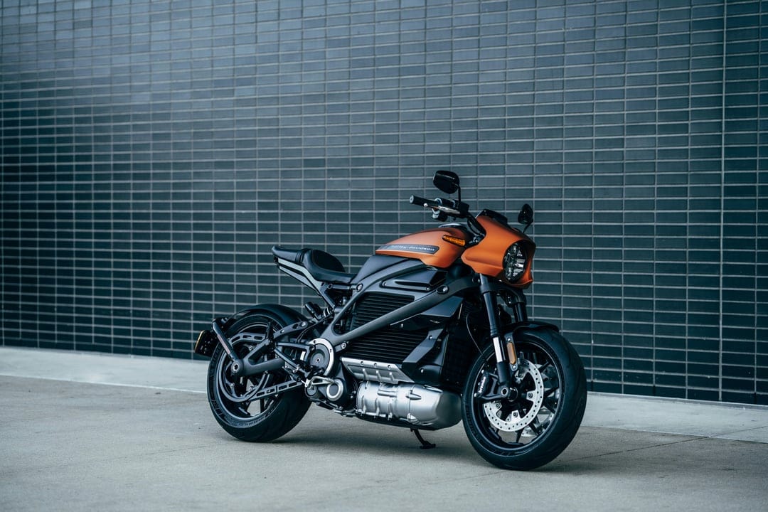Orange and black Harley-Davidson LiveWire electric motorcycle parked on concrete before a dark textured brick wall.