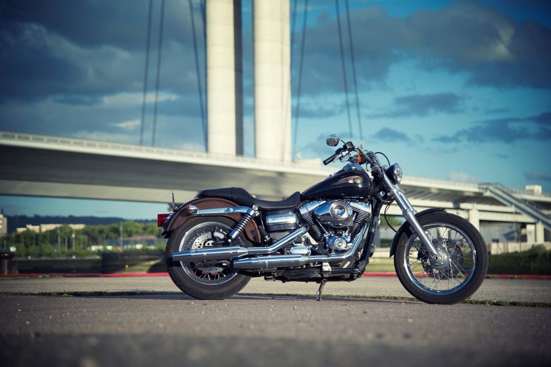 Harley Davidson cruiser with chrome details and leather bags parked under concrete bridge pylons against clouds.