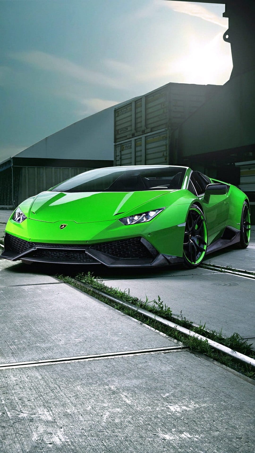 Bright green Lamborghini Huracan parked on concrete near blue cargo containers under a clear afternoon sky.