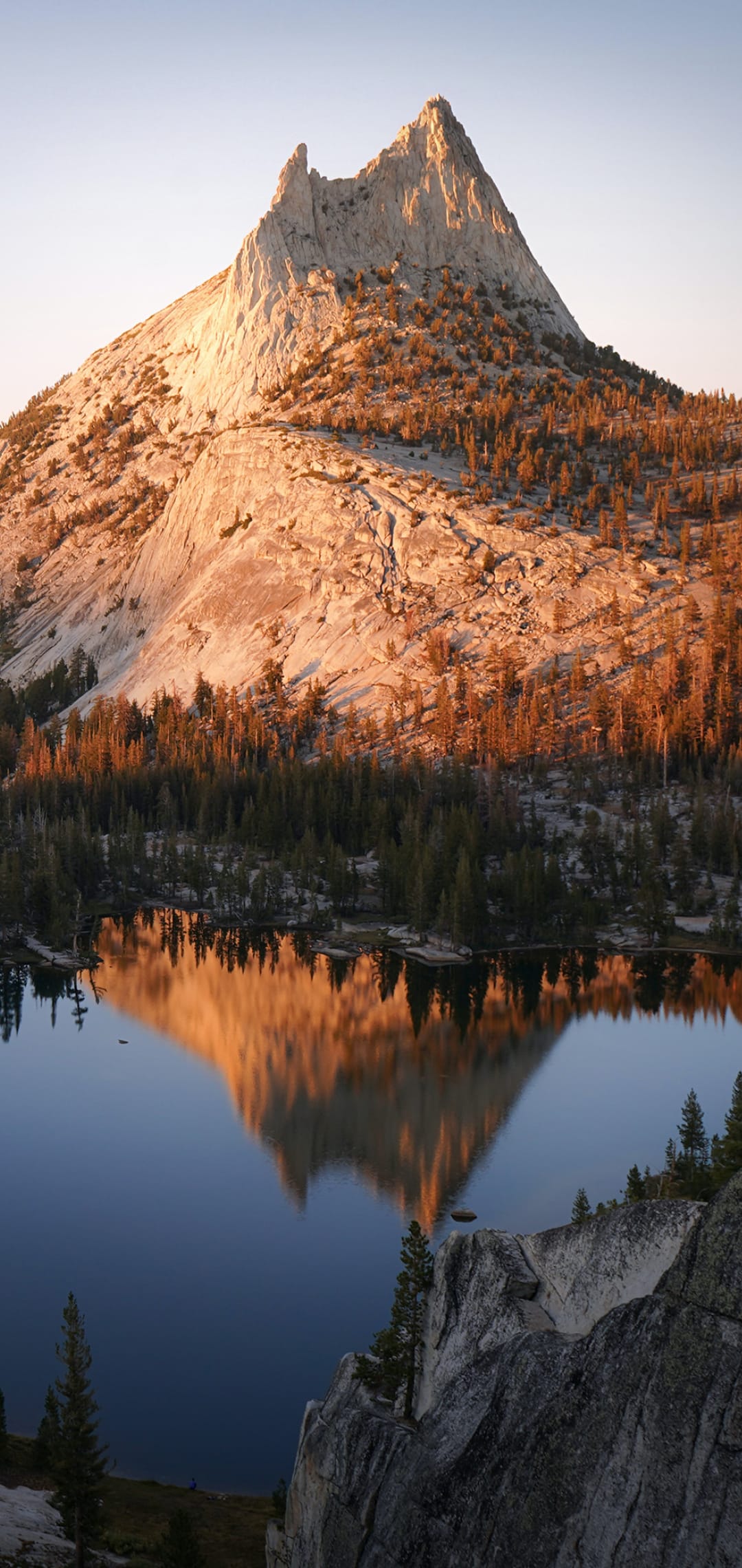 Cathedral Peak mountain with a granite summit reflecting in a still alpine lake during a golden Yosemite sunrise.