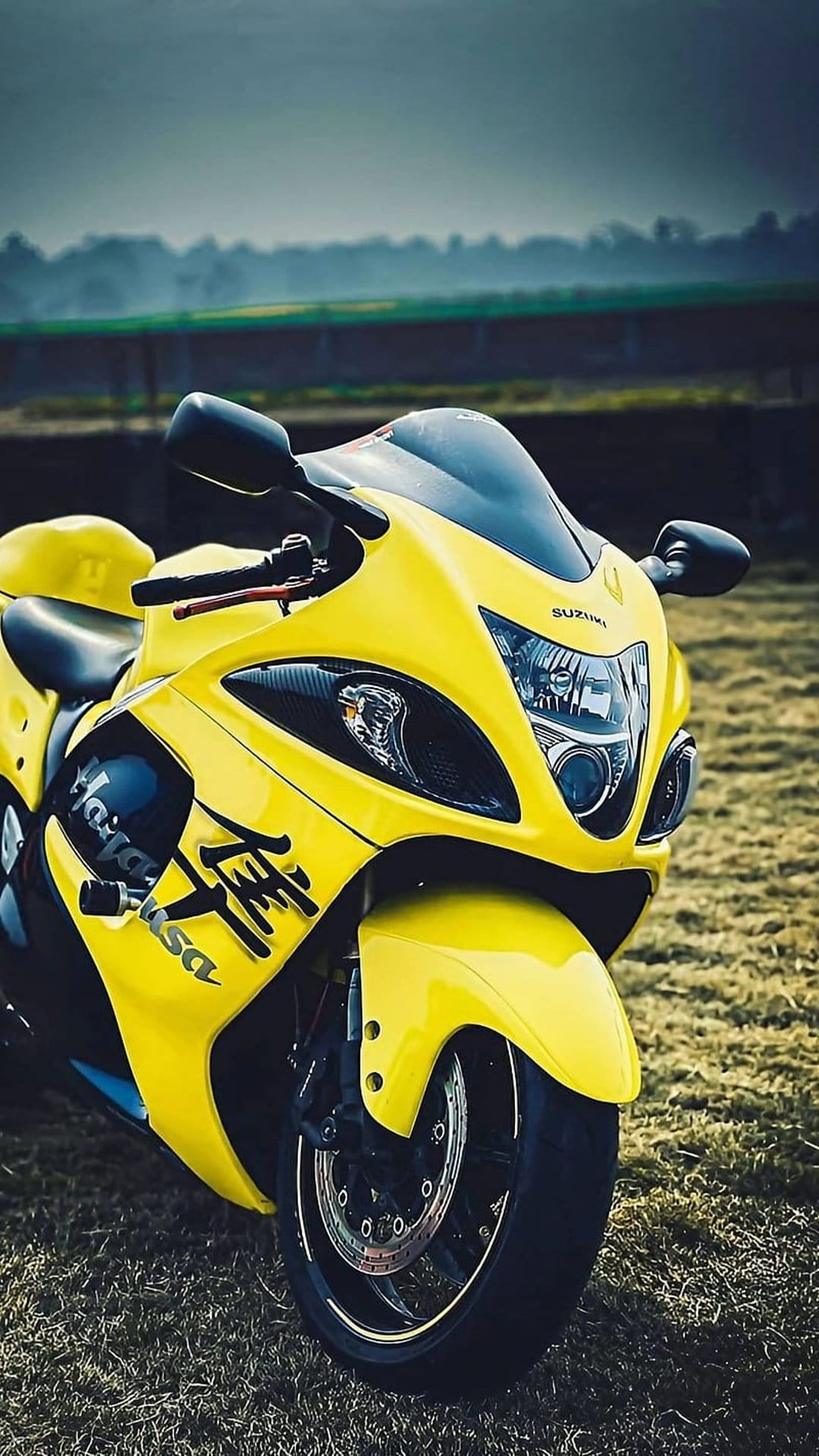 Yellow Suzuki Hayabusa motorcycle parked in a dry grassy field with blurred hills under a hazy, bright sky.