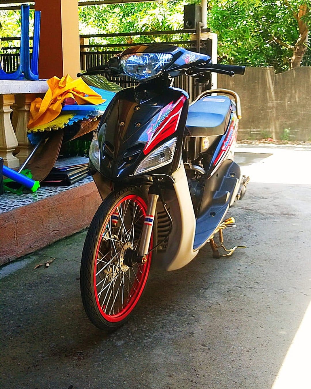 Custom black scooter with red spoked rims and flag decals parked on a concrete patio with blue chairs behind.