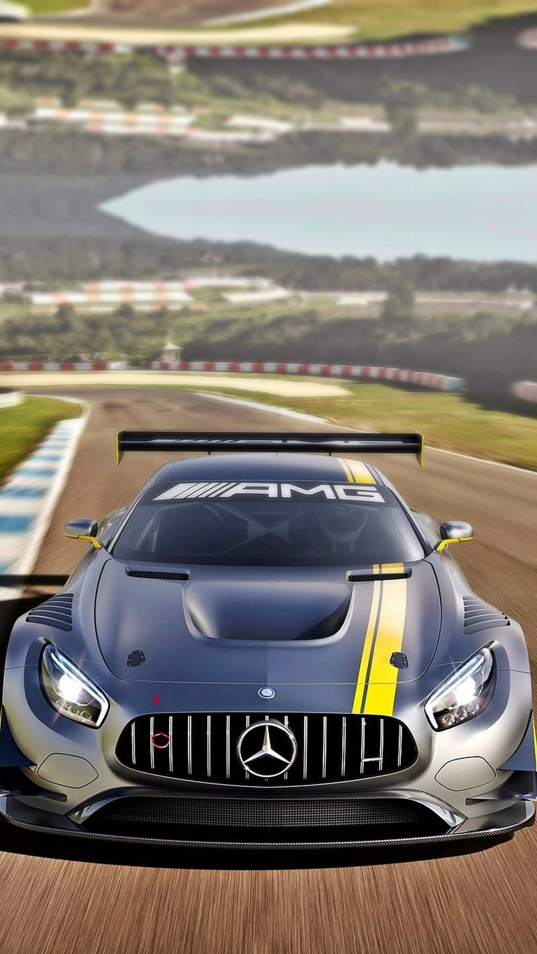 Mercedes-AMG GT racing car with yellow stripes and a rear spoiler speeds on a sunlit track with AMG logo visible.