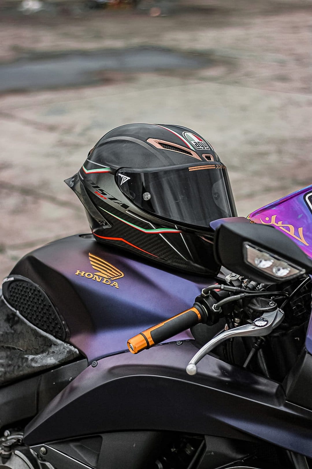 Black racing helmet with Italian flag accents resting on an iridescent purple Honda motorcycle fuel tank.