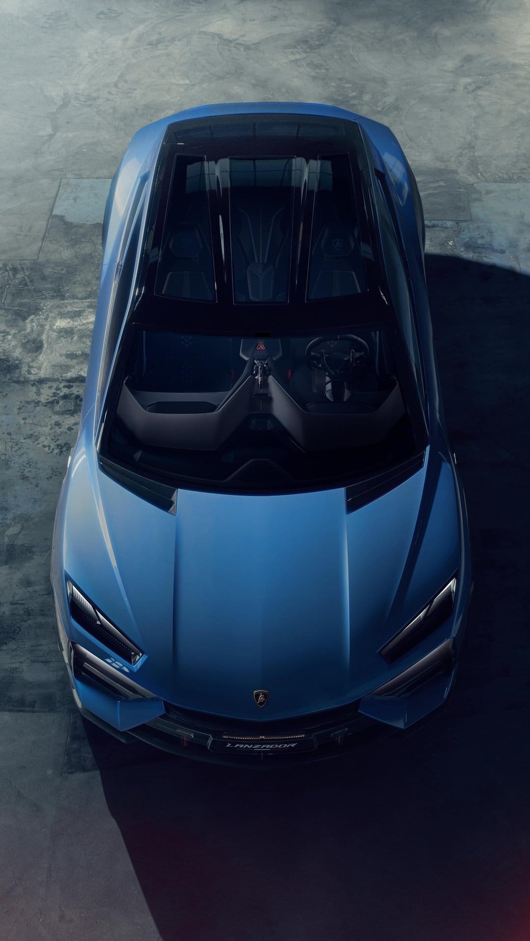 Blue Lamborghini supercar viewed from above on concrete, showing its aerodynamic shape and glass roof.