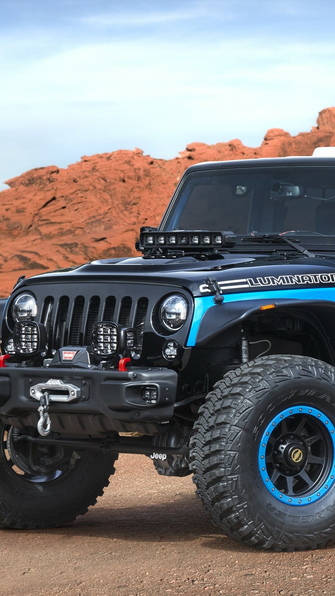 Black Jeep Wrangler Luminator with LED lights and blue beadlock wheels against red desert rock formations.