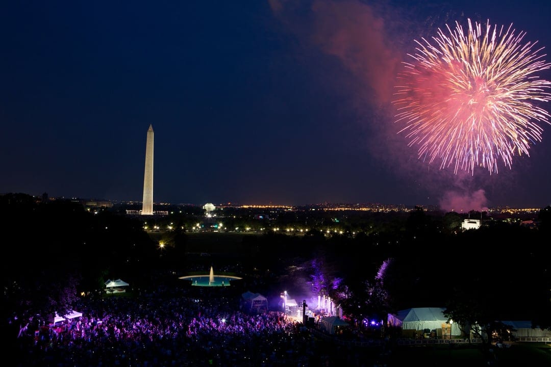 Washington Monument and U.S. Capitol under a night sky filled with colorful fireworks above a crowded city mall.