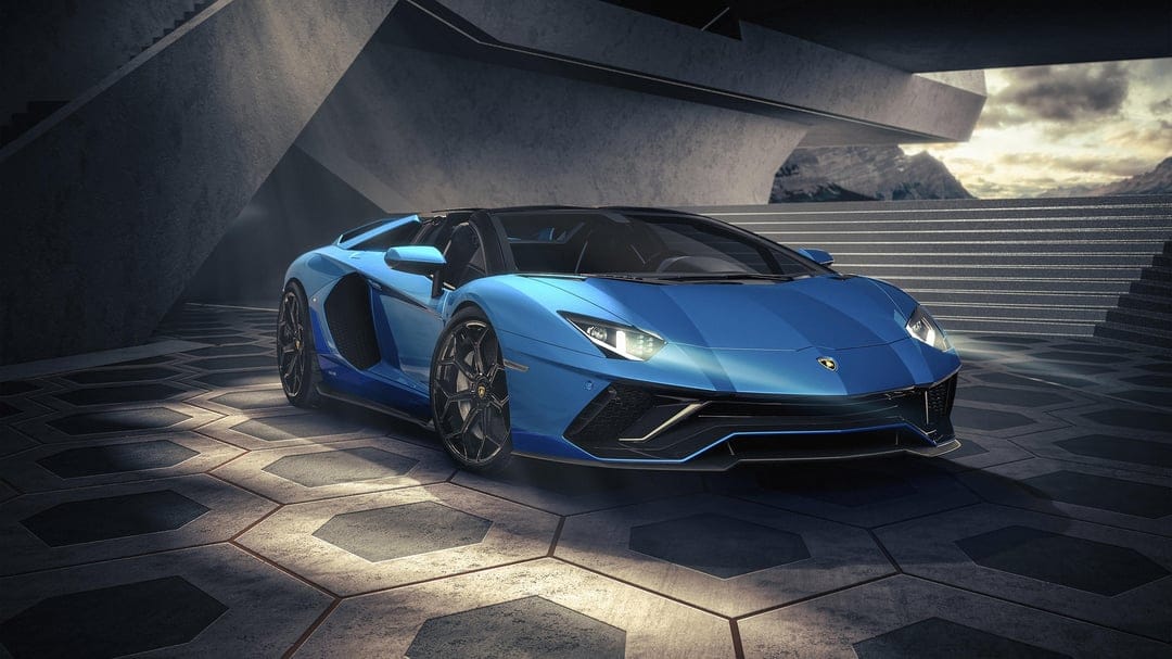 Blue Lamborghini Aventador parked on hexagonal pavement inside a brutalist concrete structure at sunset.