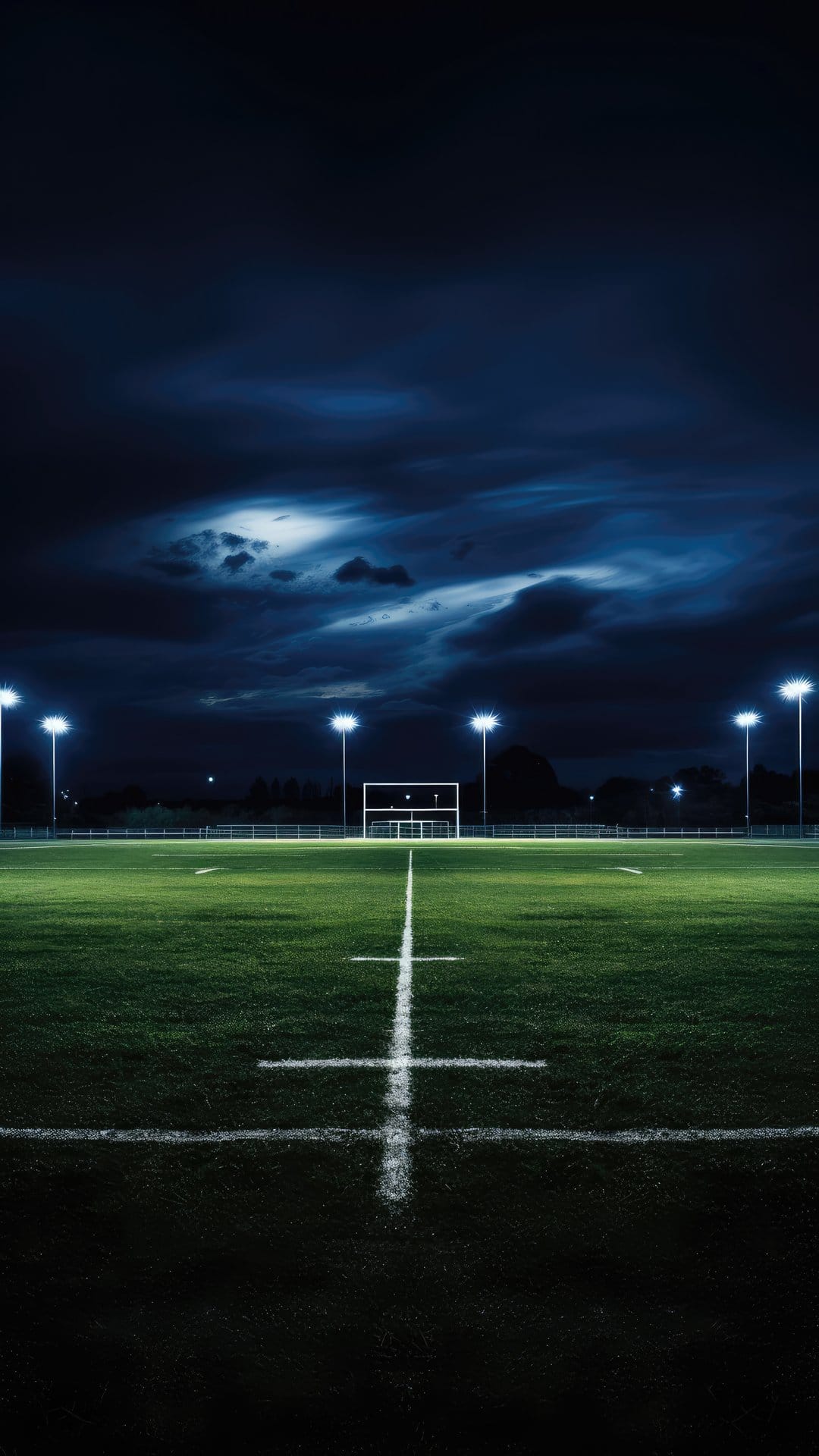 Illuminated green football field yard lines under a dark stormy night sky with bright white stadium floodlights.