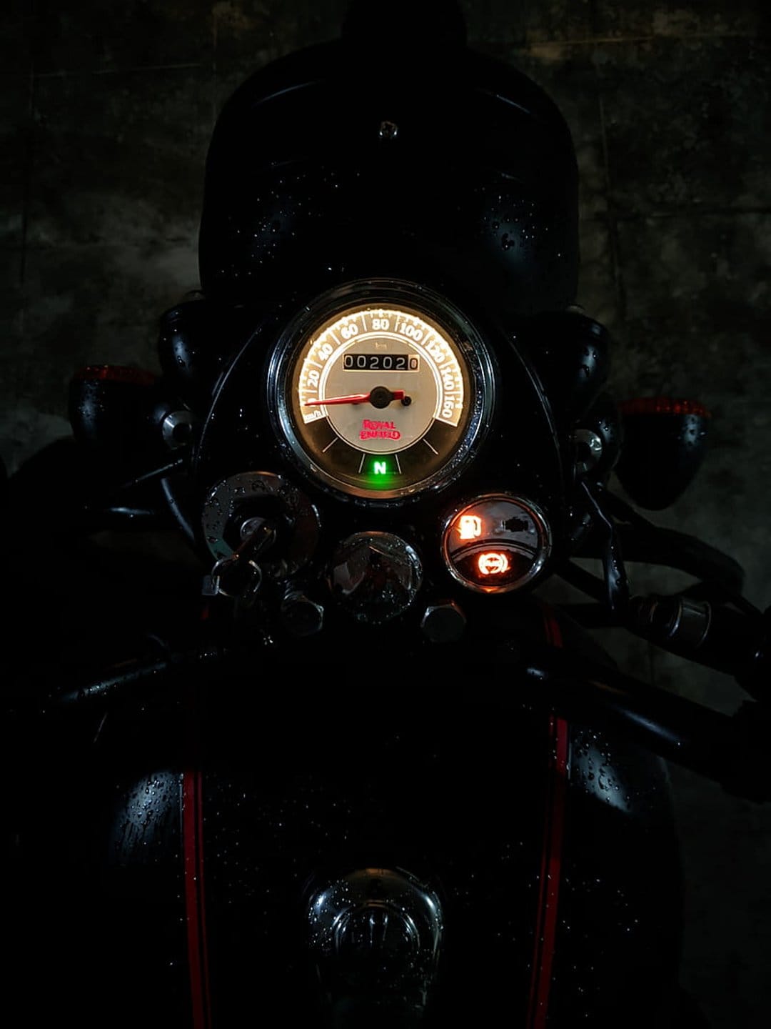 Motorcycle speedometer with glowing amber numbers and chrome housing captured in a low-light night environment.