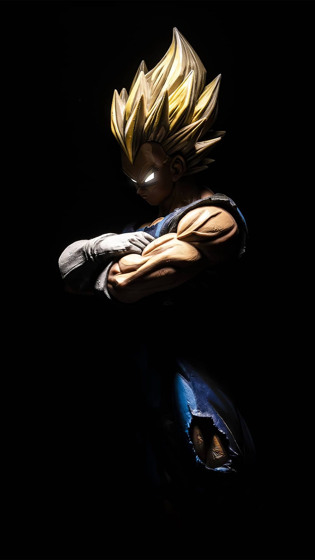 Vegeta figurine with golden spiky hair and glowing white eyes stands with arms crossed against a black background.