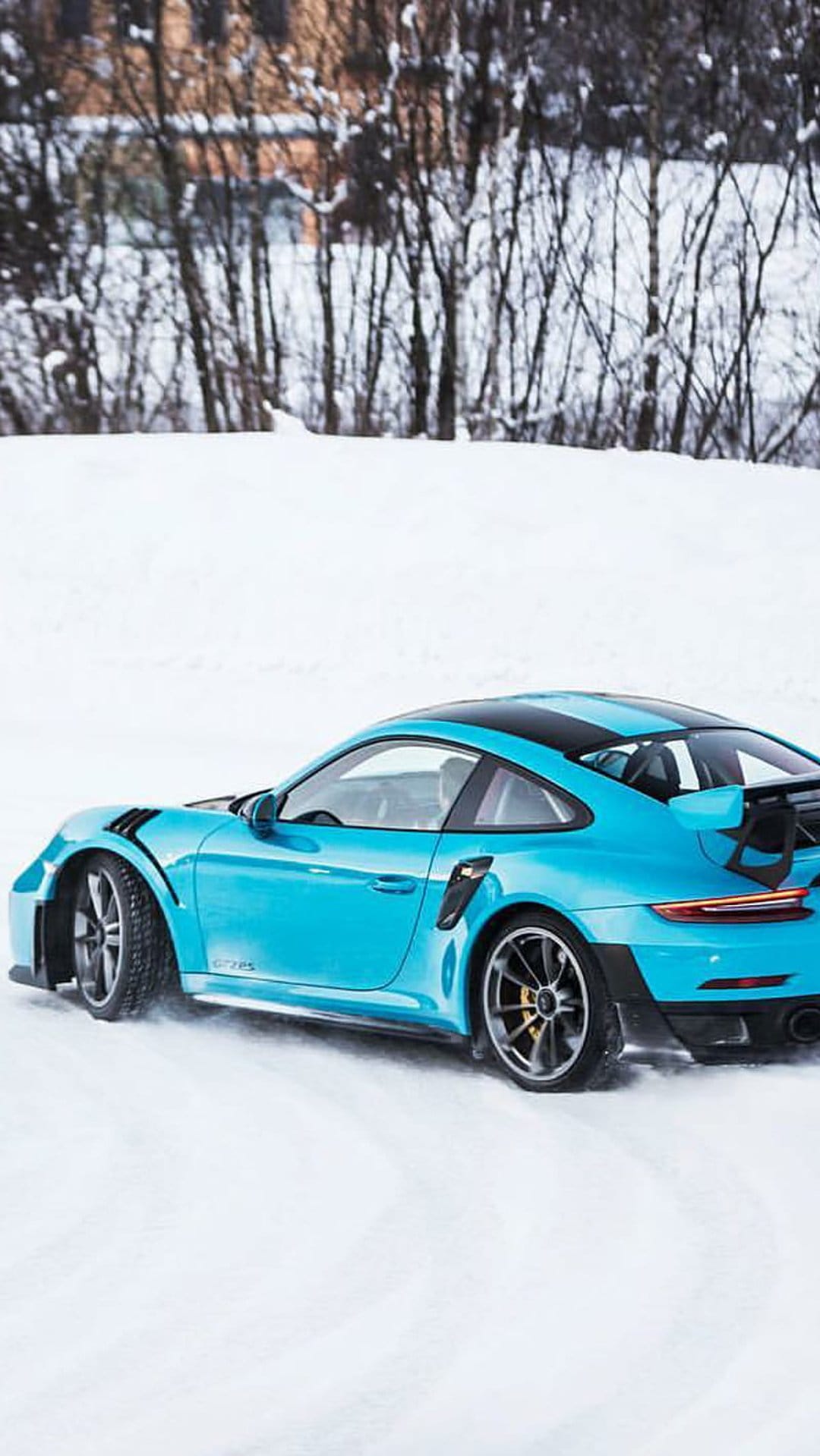 Blue Porsche 911 GT2 RS drifting on a snowy road with ice particles flying behind the rear wheels during winter.