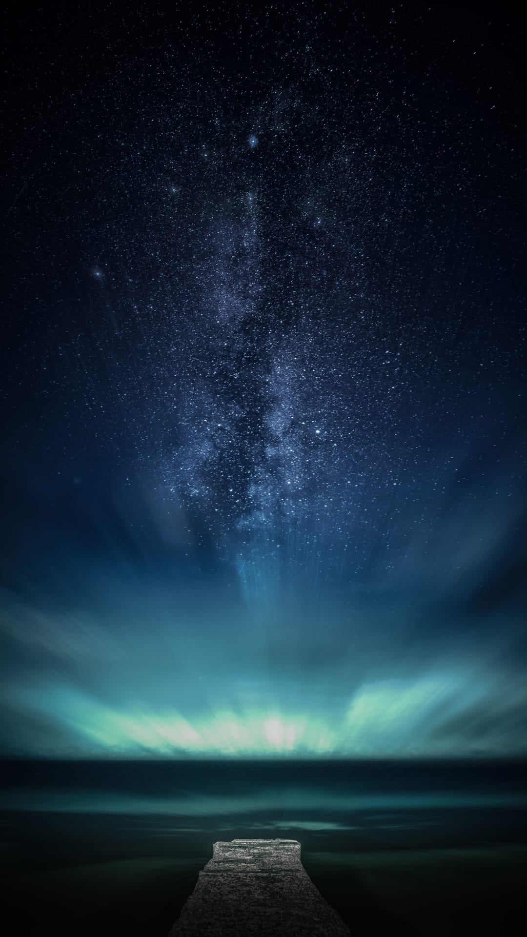Stone pier extending into calm water under a vivid Milky Way galaxy with purple and blue nebula clouds.