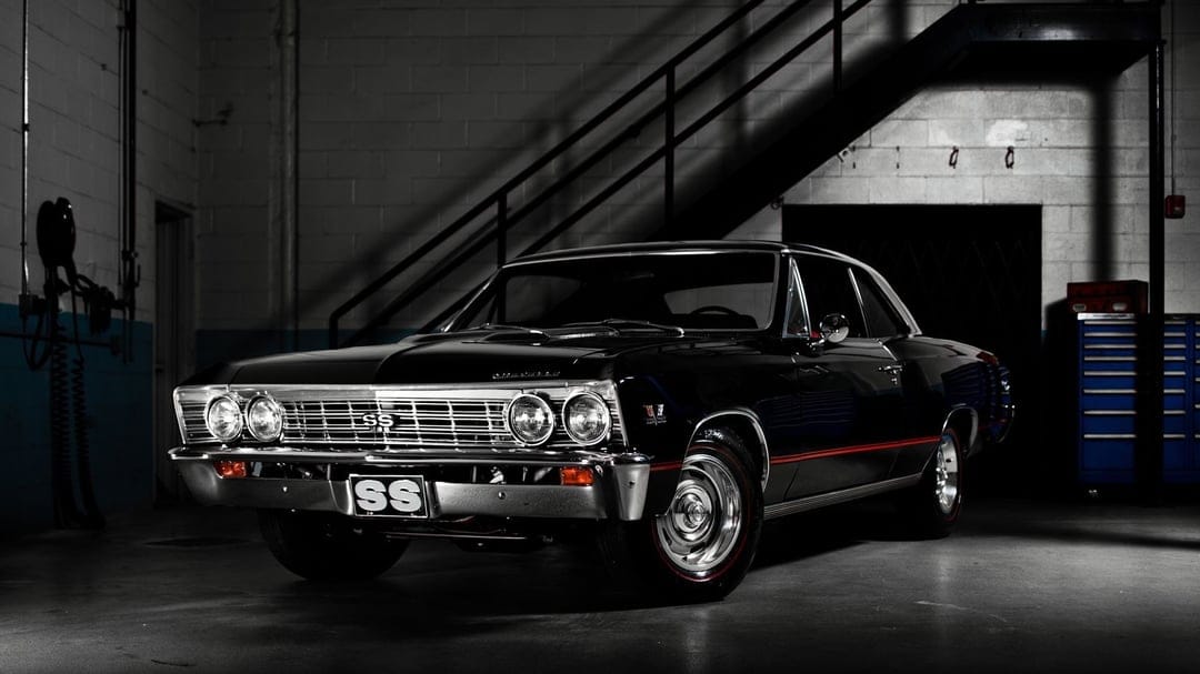 Black 1967 Chevrolet Chevelle SS parked in a dark industrial garage with dramatic lighting and chrome accents.