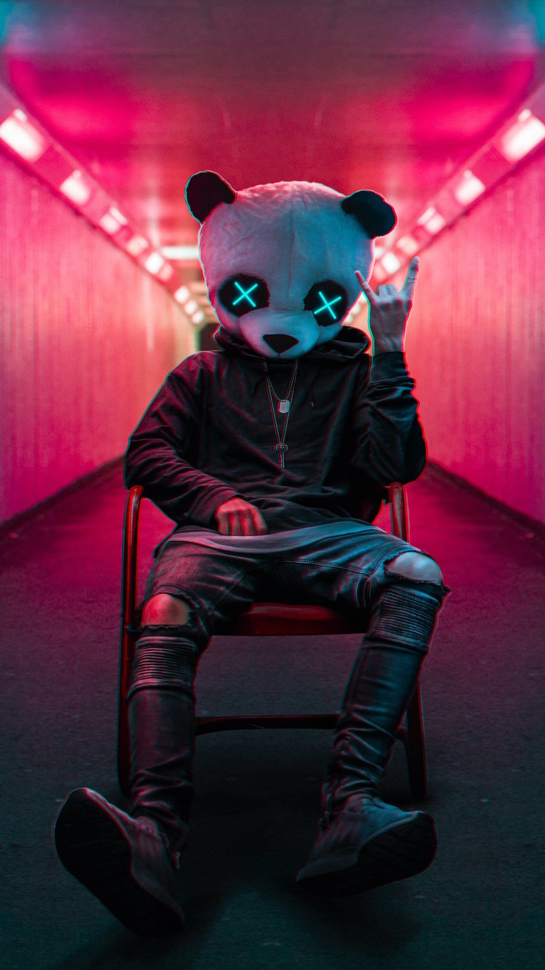 Person in a panda mask with glowing blue eyes sits in a red chair within a pink and blue neon tunnel.