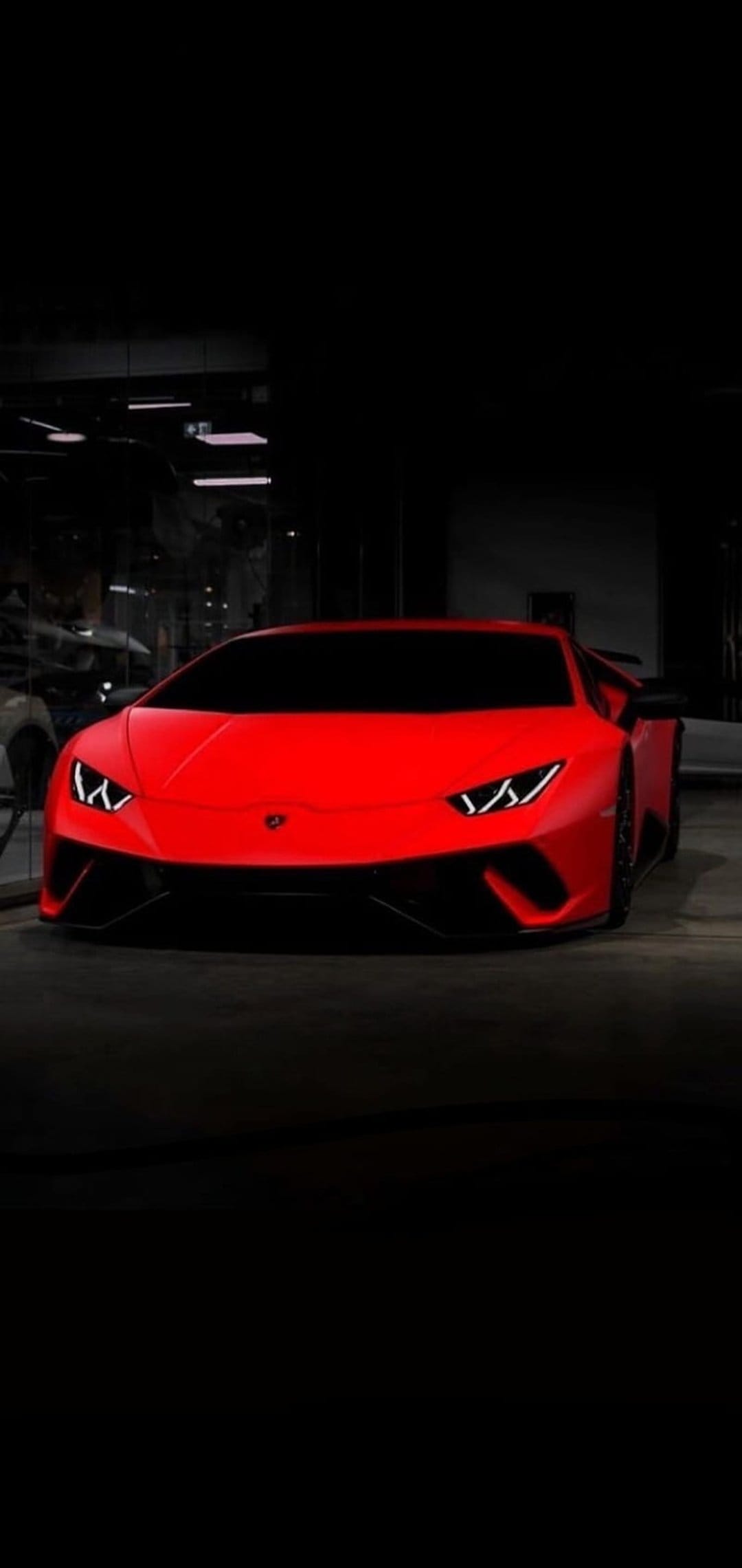 Red Lamborghini Huracan supercar in a dark showroom with glowing LED headlights and sharp aerodynamic body lines.