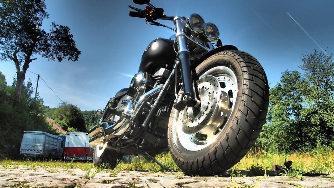 Black cruiser motorcycle with chrome accents on a stony rural road under a bright blue sky with wispy clouds.