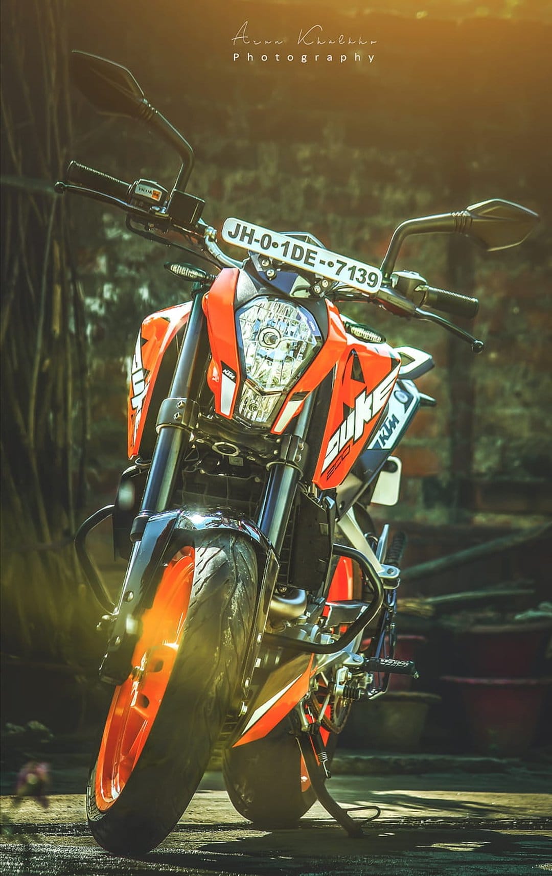 Orange KTM motorcycle front view showing the headlight, handlebars, and license plate in warm outdoor lighting.