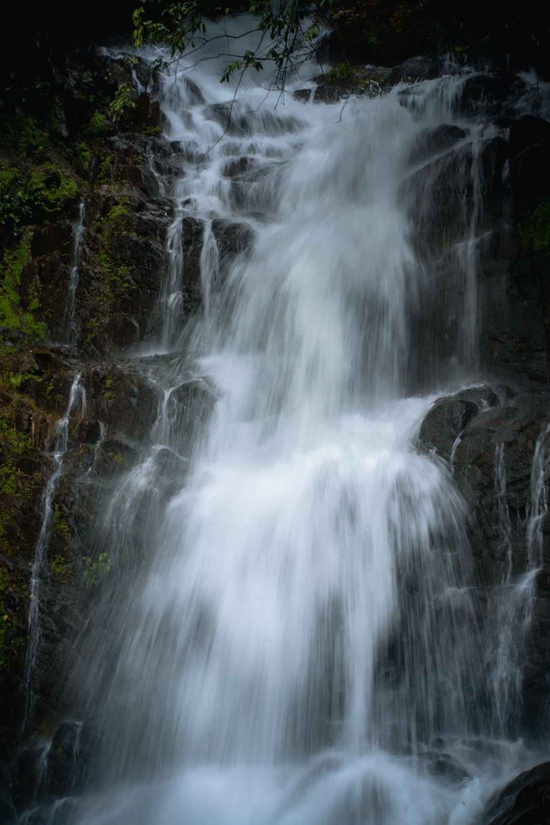 Tiered waterfall with silk-like water flowing over mossy rocks amidst a sun-drenched woodland landscape.