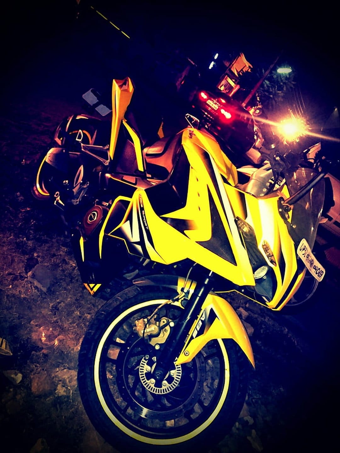 Yellow sport motorcycle with glowing headlights parked on dark ground under dramatic nocturnal lighting.