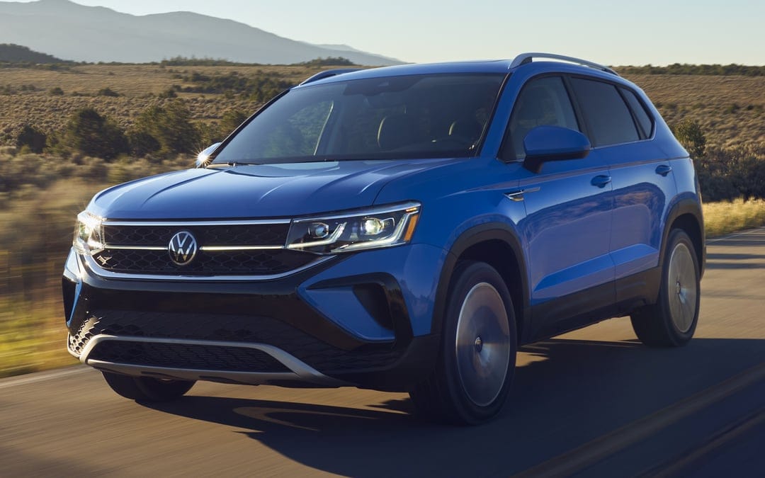 Blue Volkswagen SUV driving on a paved road through a dry landscape during golden hour with glowing LED headlights.