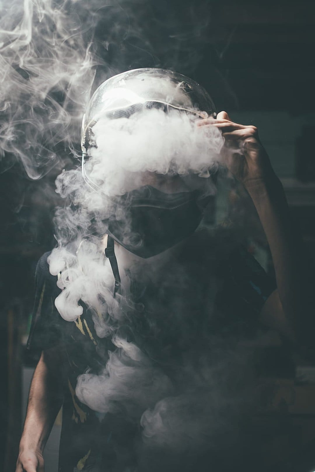 Person in a clear helmet exhales white smoke clouds against a dark background for mobile wallpaper.