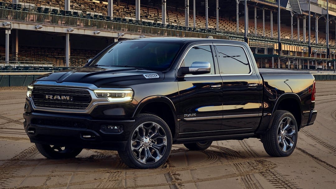 Black RAM 1500 Limited truck parked on a sand track at sunset with stadium seating in the background.