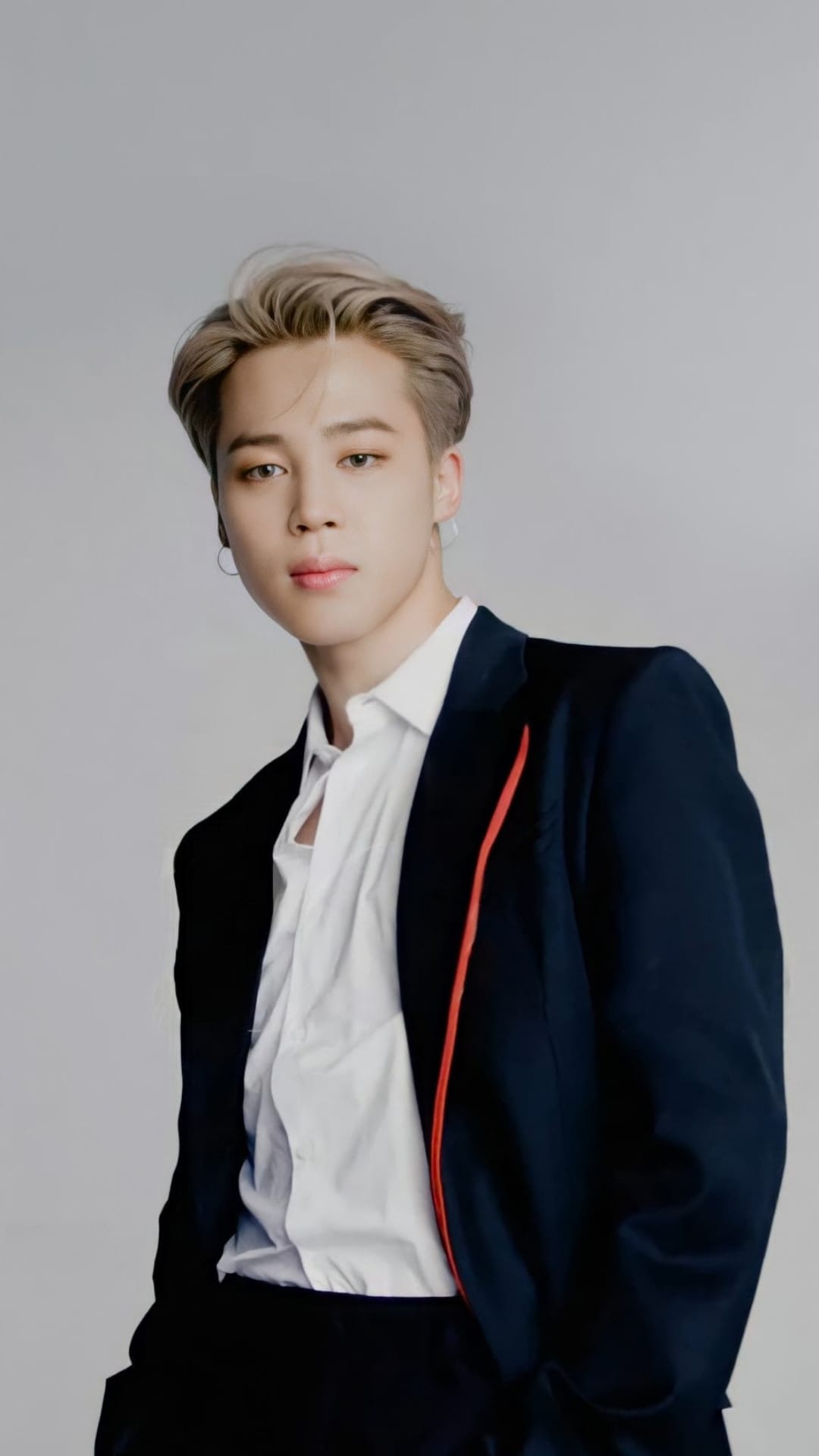 Park Jimin of BTS in a navy blazer and white shirt with styled blonde hair looking directly at the viewer.