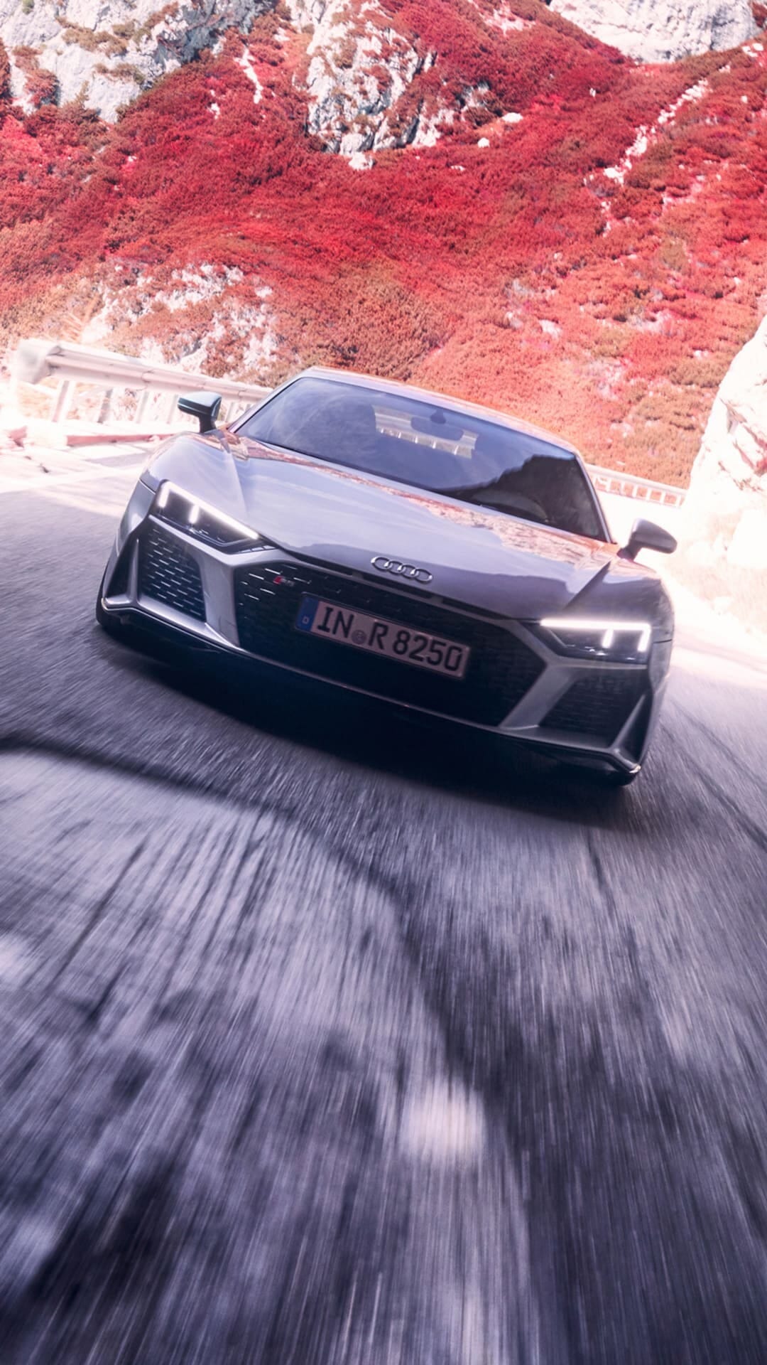 Silver Audi R8 driving fast on a mountain road with motion blur and red autumn foliage in the background.