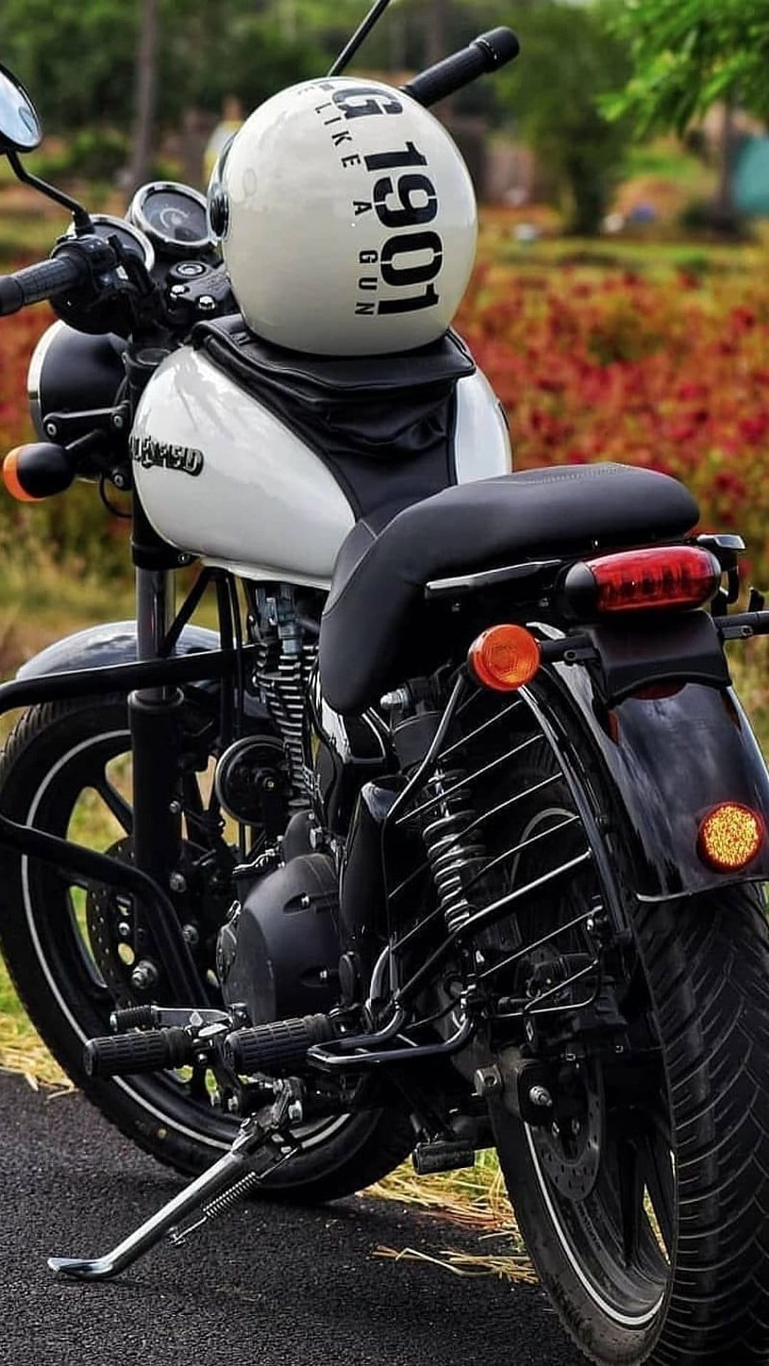 White Royal Enfield motorcycle with a vintage helmet on the tank against blurred red and green foliage.